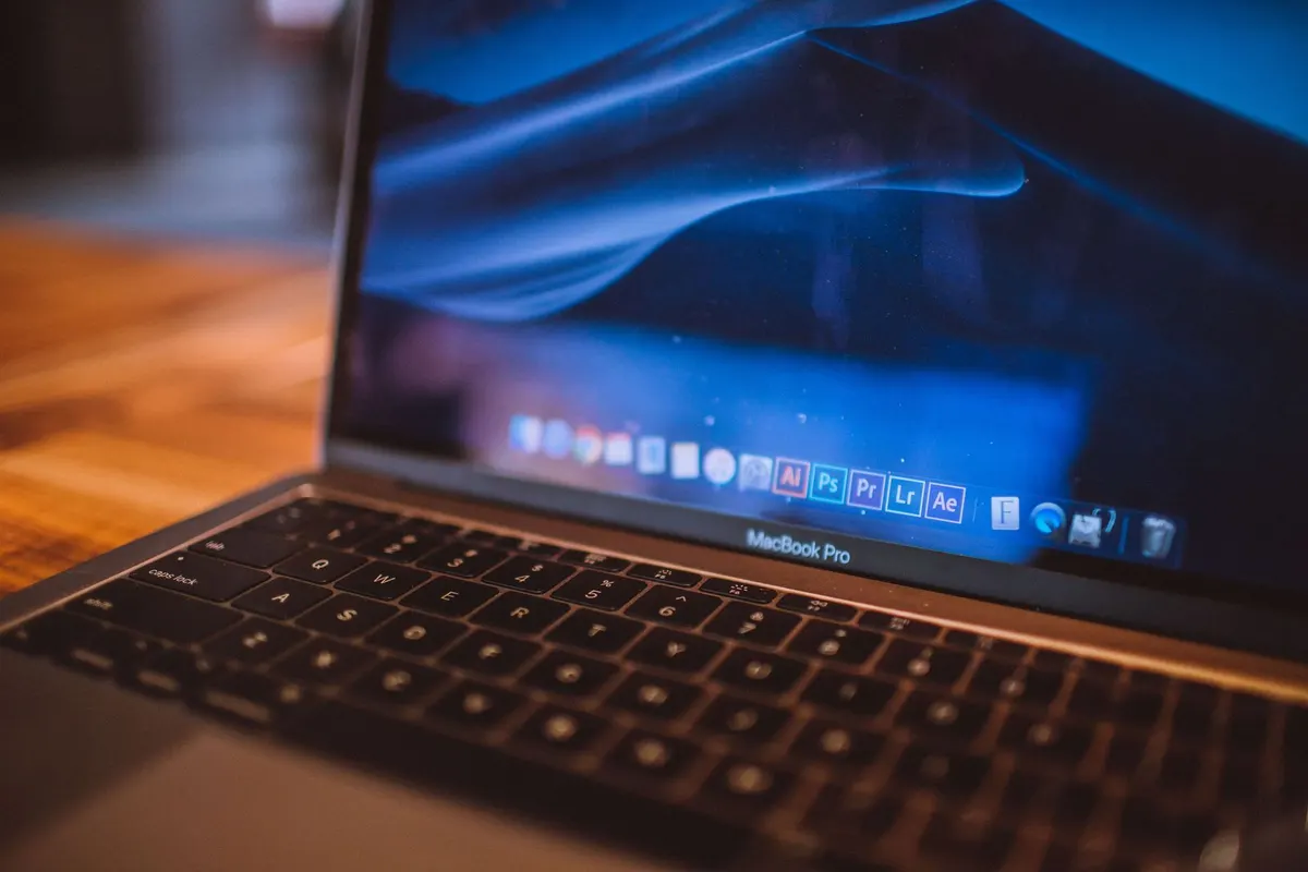 MacBook Pro aberto sobre uma mesa de madeira, tela acesa em ambiente de trabalho com pouca luz